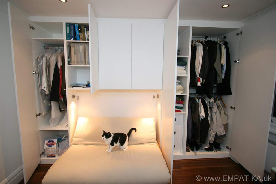 Open door view of ceiling high wardrobes painted White with a cat on a sofa bed in the alcove