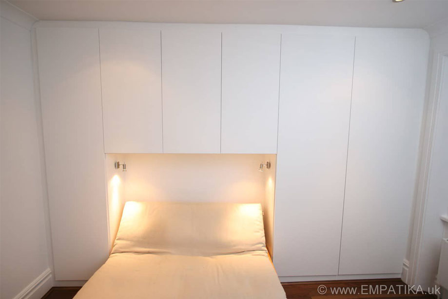 Full view of bespoke wardobes painted White with no handles and a sofa bed in the alcove with lighting