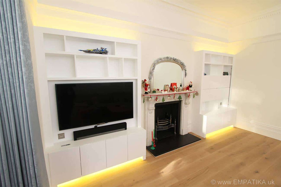 2 Large, White painted media units with sliding cover for wall-mounted TV, accent top and bottom lighting and a fireplace in between