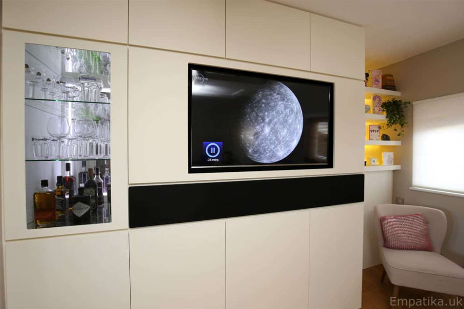 Floor to ceiling bespoke fitted media unit with wall recessed flatscreen TV in the center and wine storage closet with lights