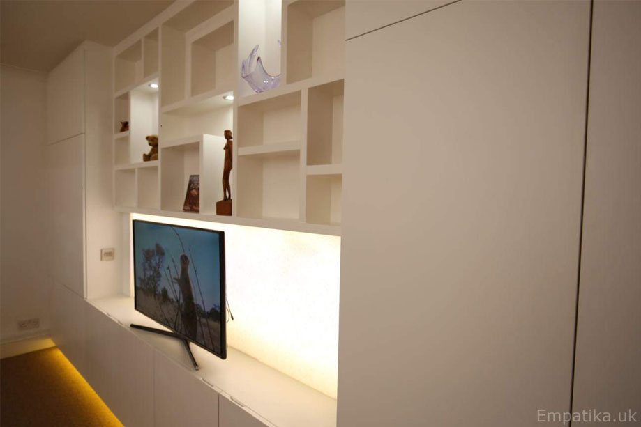 Right side view of built in fitted display unit with closets surrounding a LED panel TV stand and asymmetrical shelving with LED lights