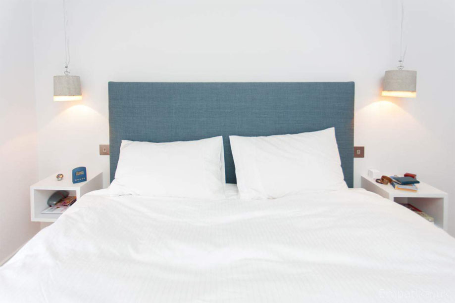 White painted floating square shelves on either side of a bed