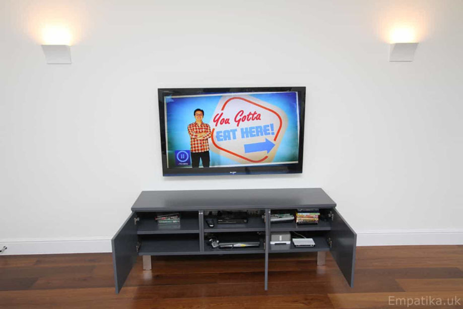 Open-door view of Gray-painted built-in media unit with shelves inside for gadgets and consoles storage