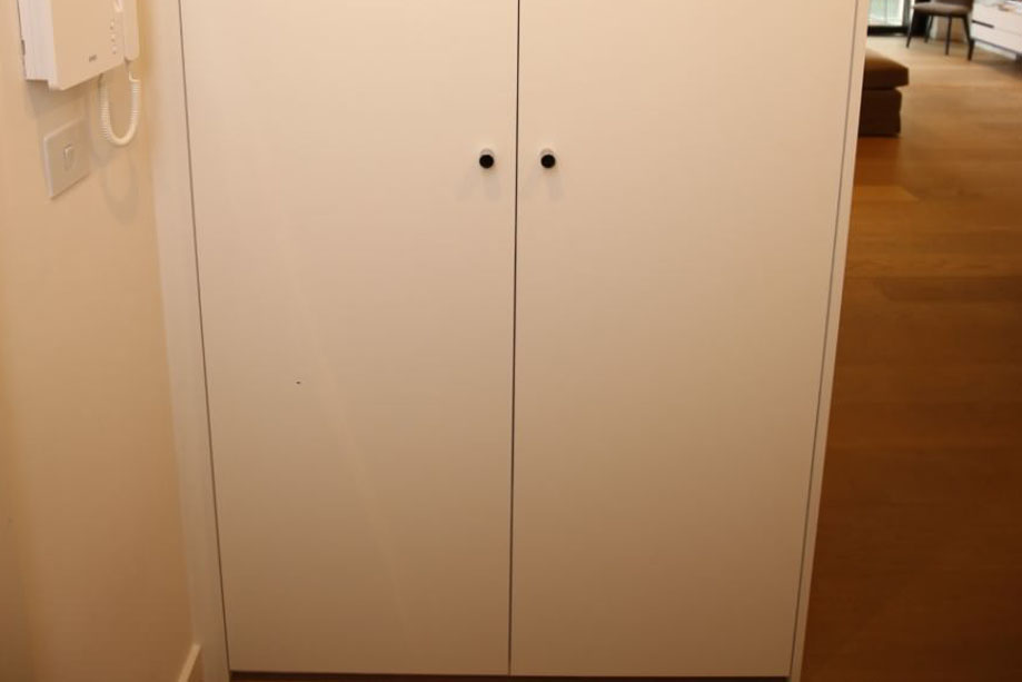 Full view of sleek hallway cupboard with 2 floor to ceiling doors painted White with small steel handles