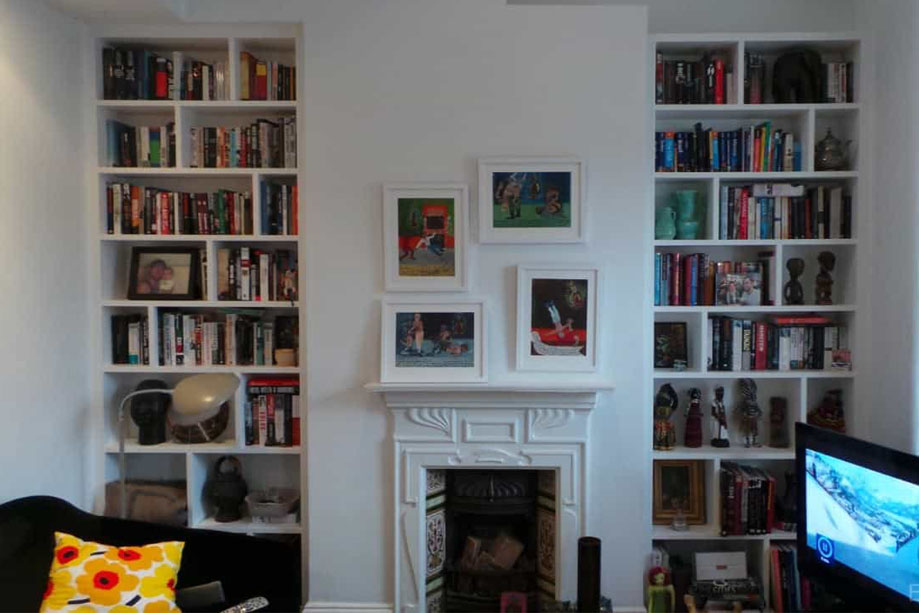 Full view of 2White painted fitted alcove bookcases on recessed walls with a fireplace in between