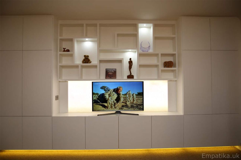 Full view of modern built in storage unit with TV media stand and LED light asymmetrical shelves in the middle alcove