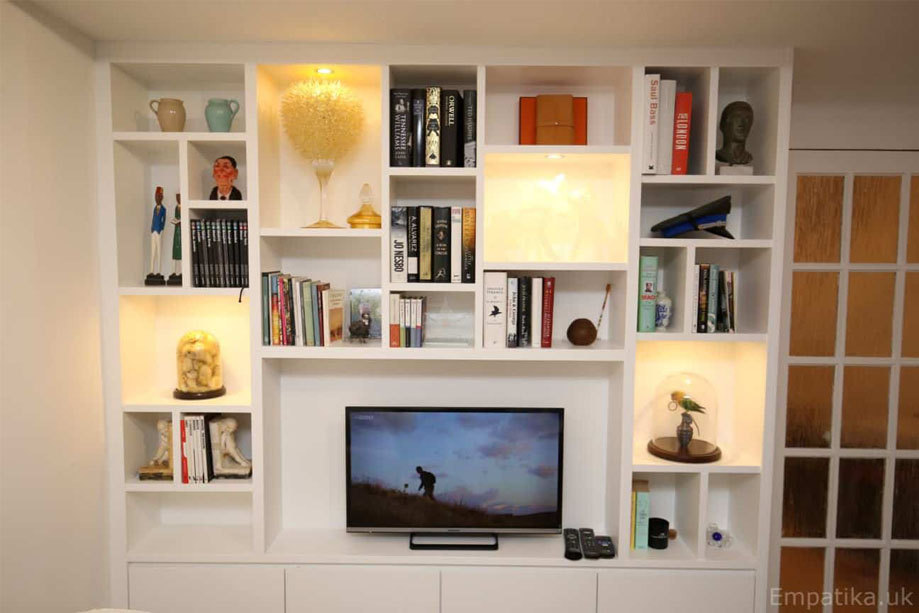 Tall display unit painted White with shelves surrounding a TV stand and 4 storage closets on the bottom