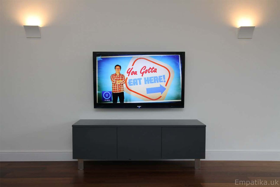 Gray painted media unit with 3 doors, wall-mounted TV above and 2 accent lights on either side