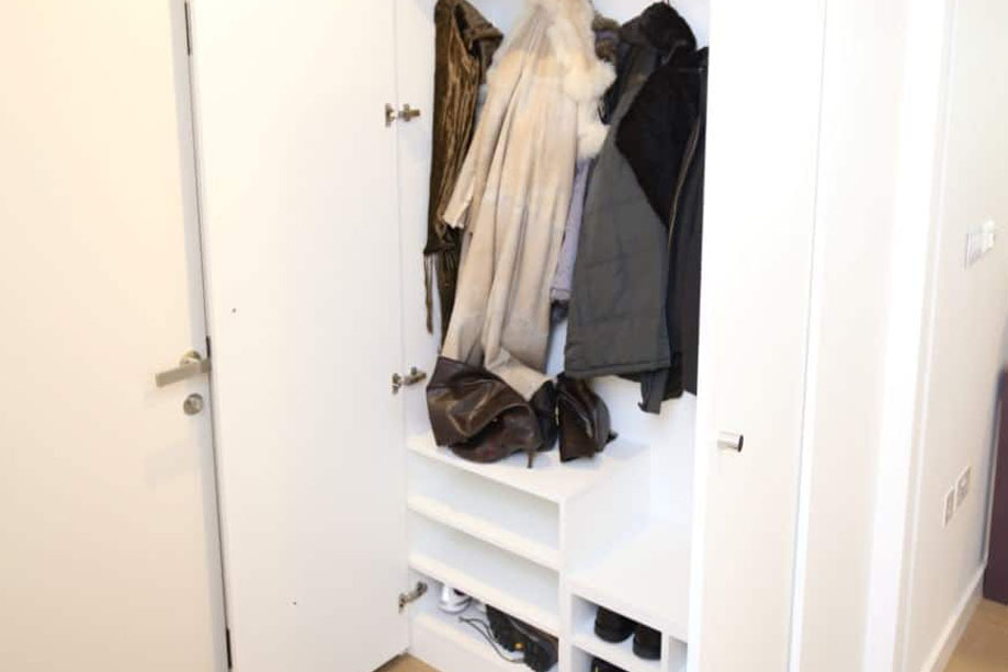 Interiors of custom fitted 2-door storage closet for coats and shoes with shelves and hooks by the hallway