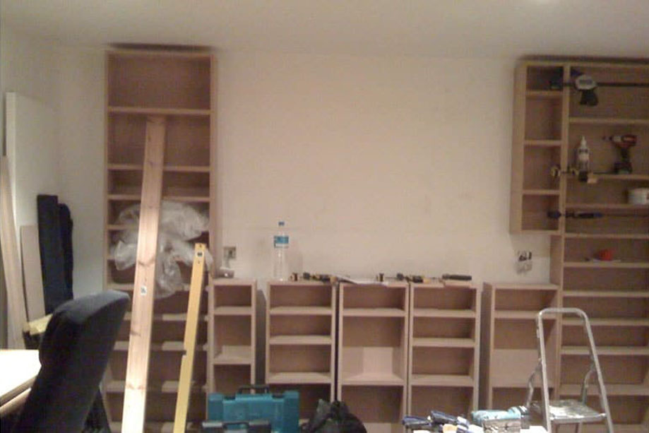 Installation of prefinished library bookcase with shallow vertical shelves on a bare wall