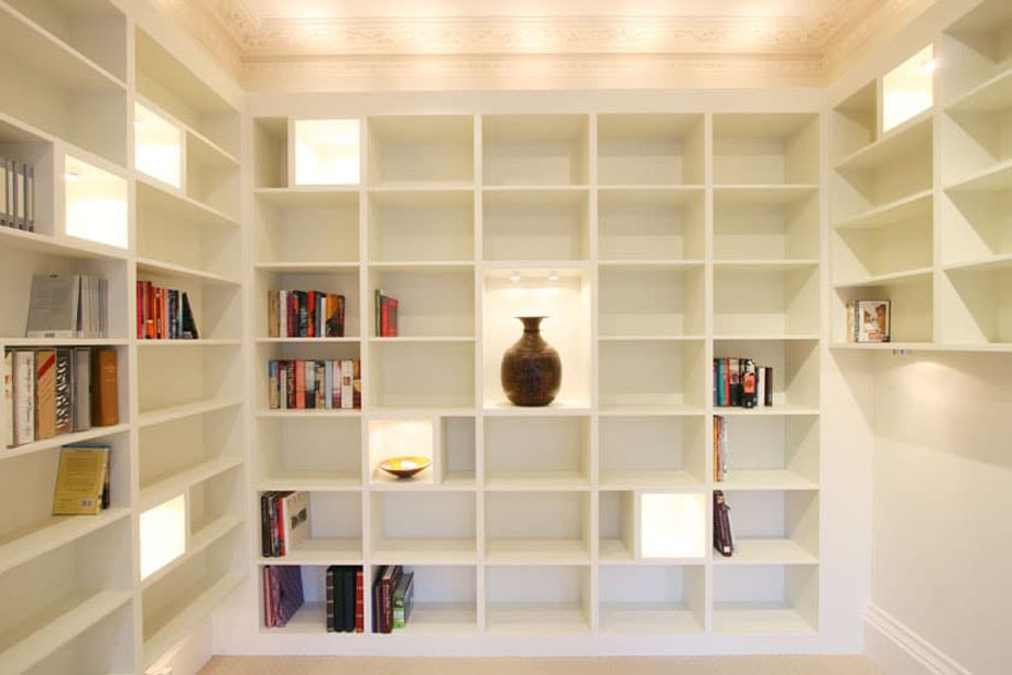 Tall White painted bookcases on 3 walls with LED light accent square shelves