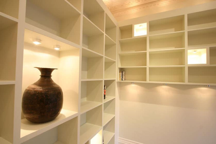 Side view of tall White painted bookcase with accent shelves LED lights and a matching smaller unit on corner wall