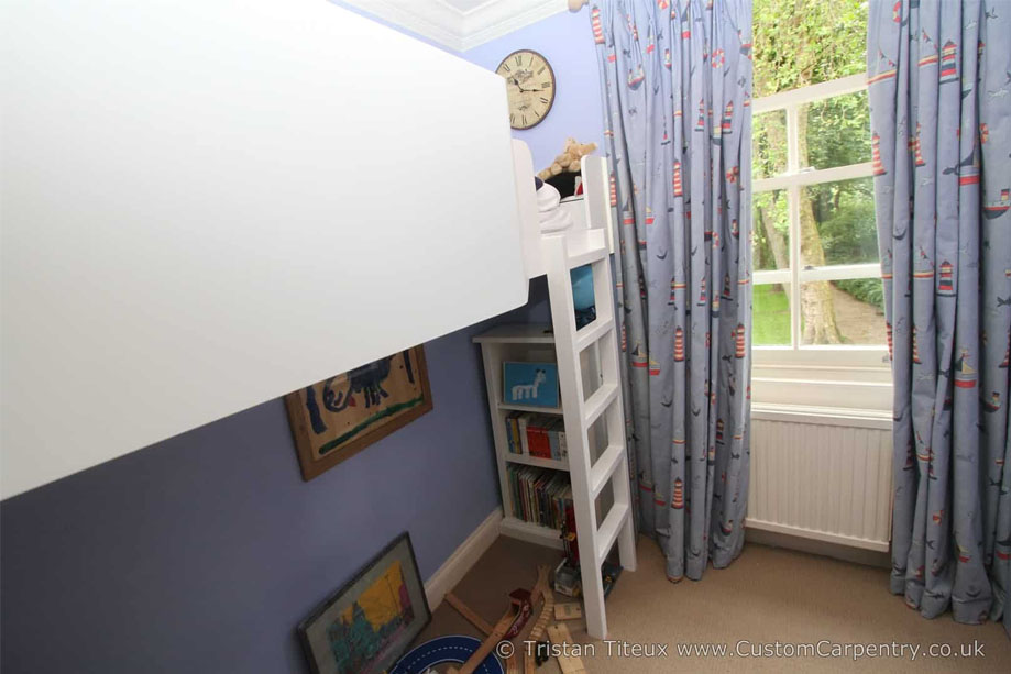 View from the door inside a children's room with White painted fitted loft bed with play area and bookcase underneath