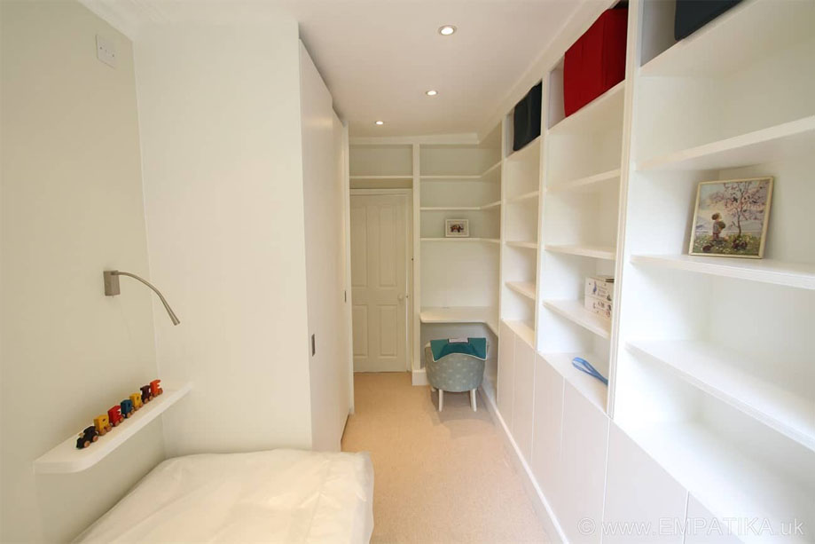 Custom floor to ceiling L-shaped shelving with bottom cupboards painted White inside children's bedroom