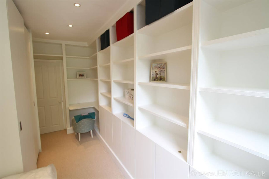 Fitted floor to ceiling White painted storage shelves with bottom closets and corner desk by the door