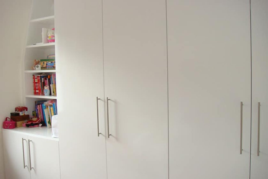 White painted bespoke wardrobes with steel bar handles and angled ceiling open shelves on the corner
