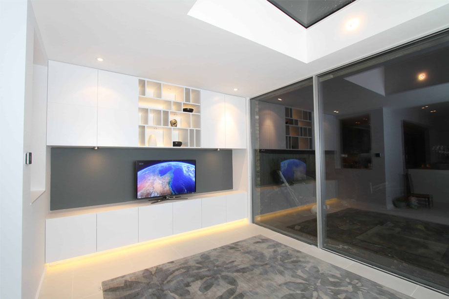 View of stylish living room with bespoke TV media unit with furniture underglow and asymmetrical shelving above