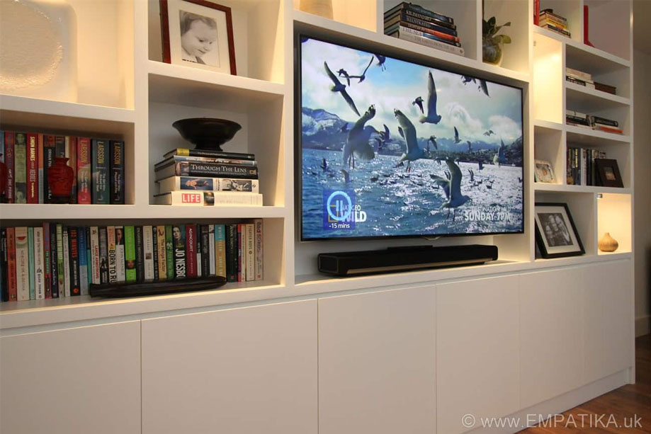 Left side close up view of bespoke White painted TV media unit with asymmetrical shelves filled with books and artwork