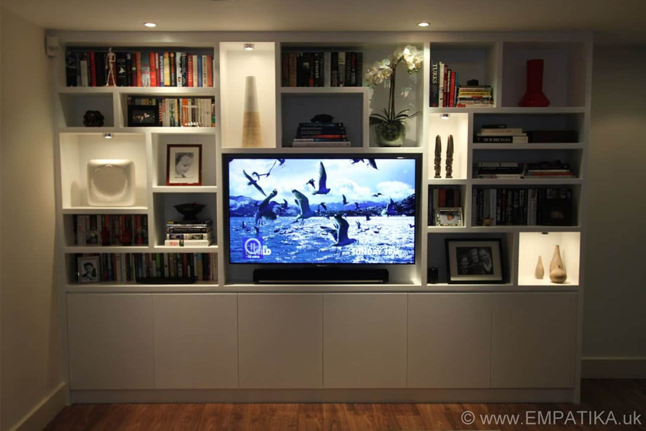 Full view of custom fitted TV media unit with bottom closets and ceiling high shelves with LED lights