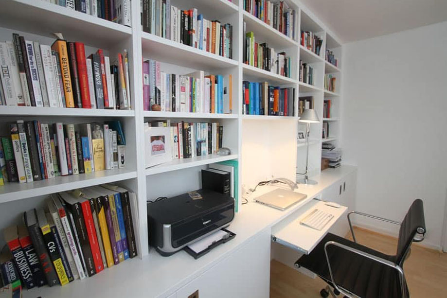 Side view of home library bookcase with shelves, bottom cabinets with doors, and a computer desk all painted White