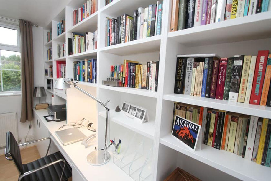 Neatly organized books on the shelves of a White painted home library bookcase with computer desk