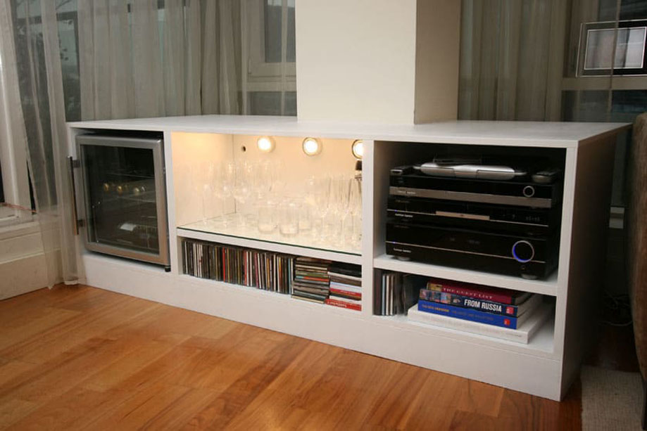 White painted low media unit with glass door wine closet, one LED light shelf, and 3 open shelves