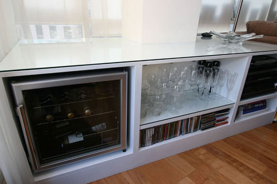Closer view of low media unit with glass tabletop, one glass door wine closet and 4 open shelves for consoles