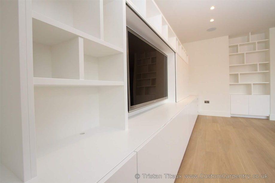 Side view of wide wall to wall TV unit with cabinets, drawers, shelves, and a wall-mounted TV with sliding cover
