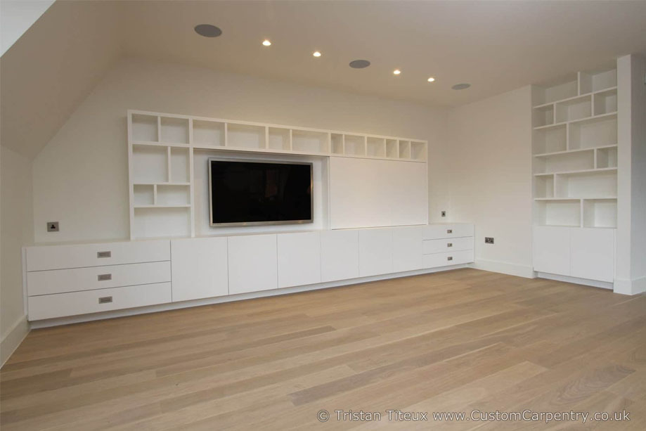 Full view of a custom made media unit with wall-mounted TV, surrounding bookcase, and matching recessed shelves on the next wall
