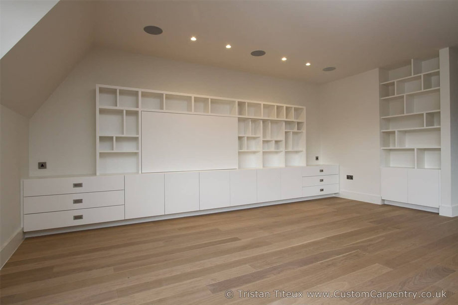 View of a room with White painted fitted media unit with shelves and a sliding cover for wall-mounted TV