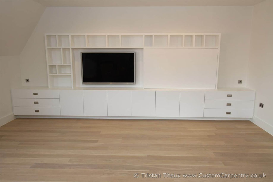 Full view of fitted media unit with wall-mounted TV in view and a sliding cover beside it, with bottom closets and drawers