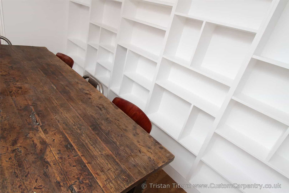 Fitted White painted bookcase with asymmetrical shelves beside wooden table