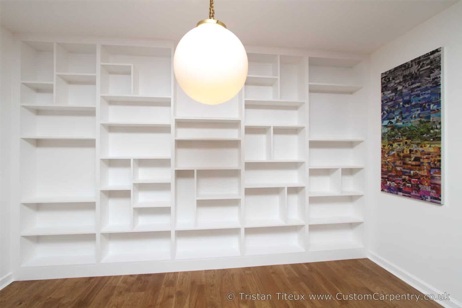 Wide built in wall to wall bookcase painted White with asymmetrical shelves