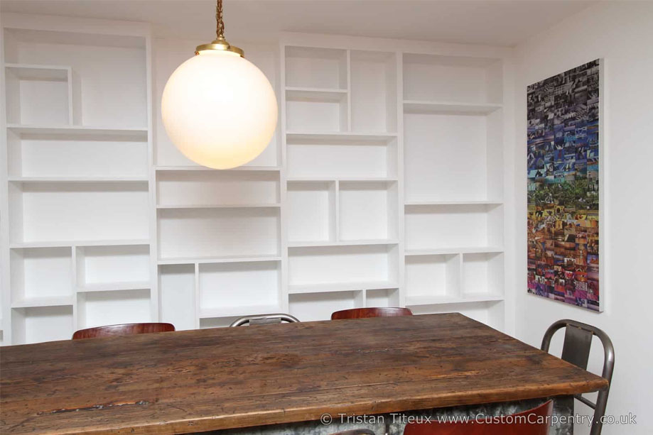 White painted library bookcase with asymmetrical shelves built on a large wall