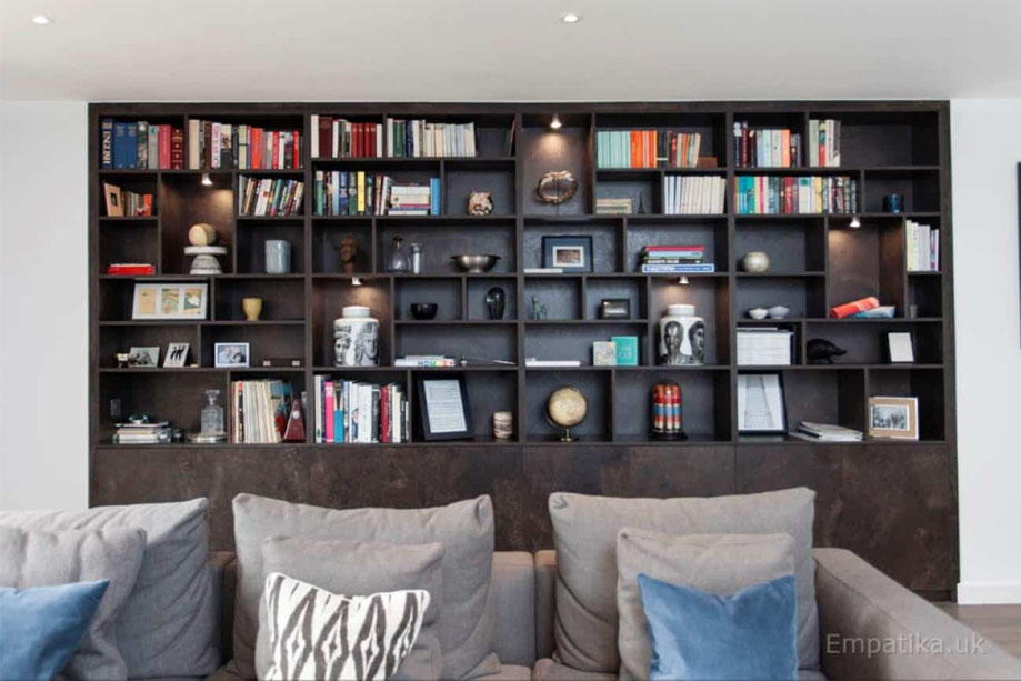 Front view of large floor to ceiling display unit with spot down LED lights on some shelves behind a tylish sofa